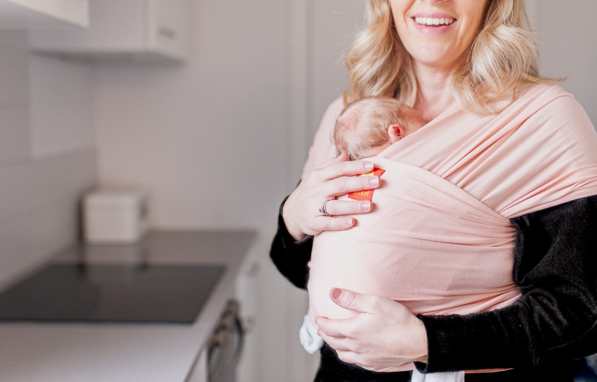 A smiling mother holds her newborn baby in a pink hana baby sling happy with her purchase