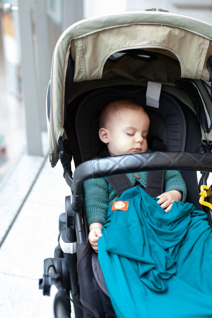 Baby sleeping in a bugaboo pram with a teal baby blanket
