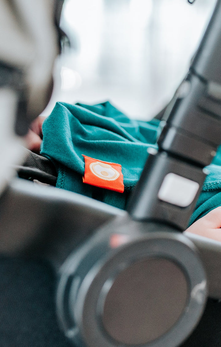 Close-up of a baby in a pram with a green blanket and orange tag.
