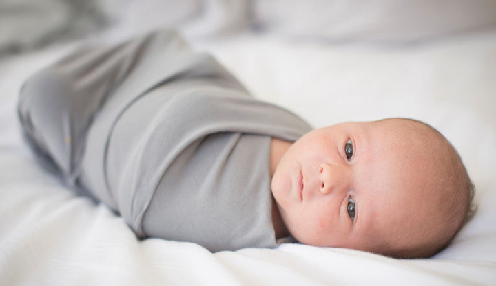 Newborn baby swaddled in gray baby swaddle on a white blanket