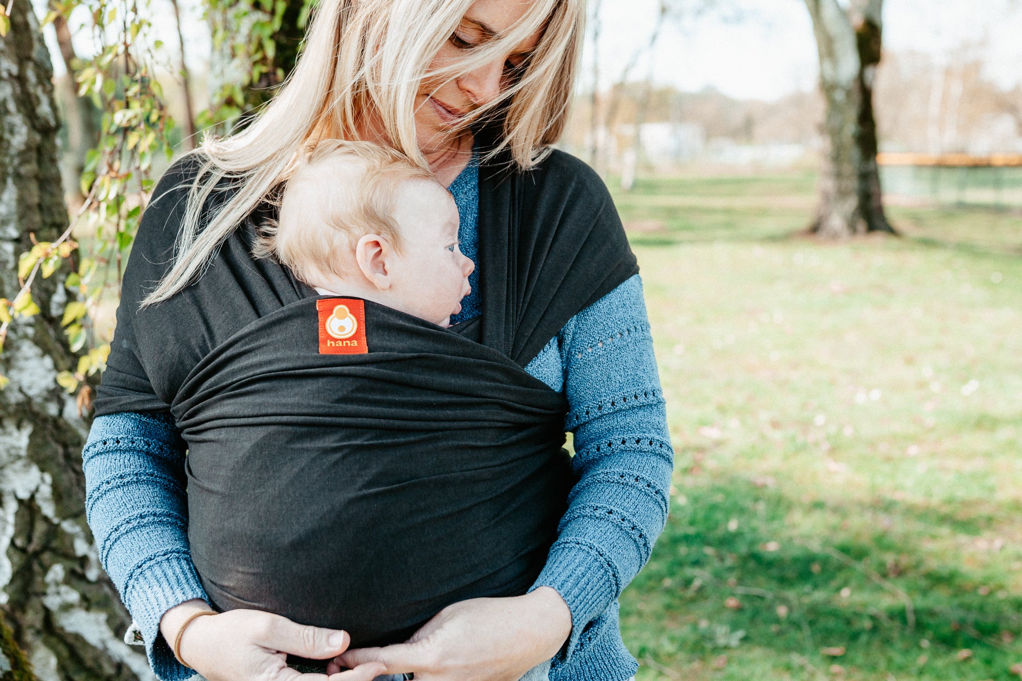 Woman carrying a baby in a sling outdoors in a park