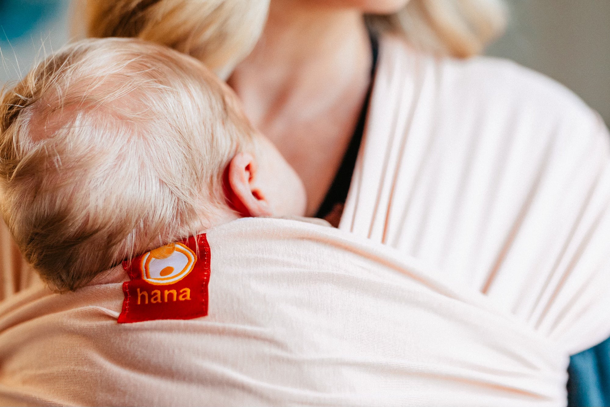 A newborn baby sleeps in a Hana Baby Pink Sling