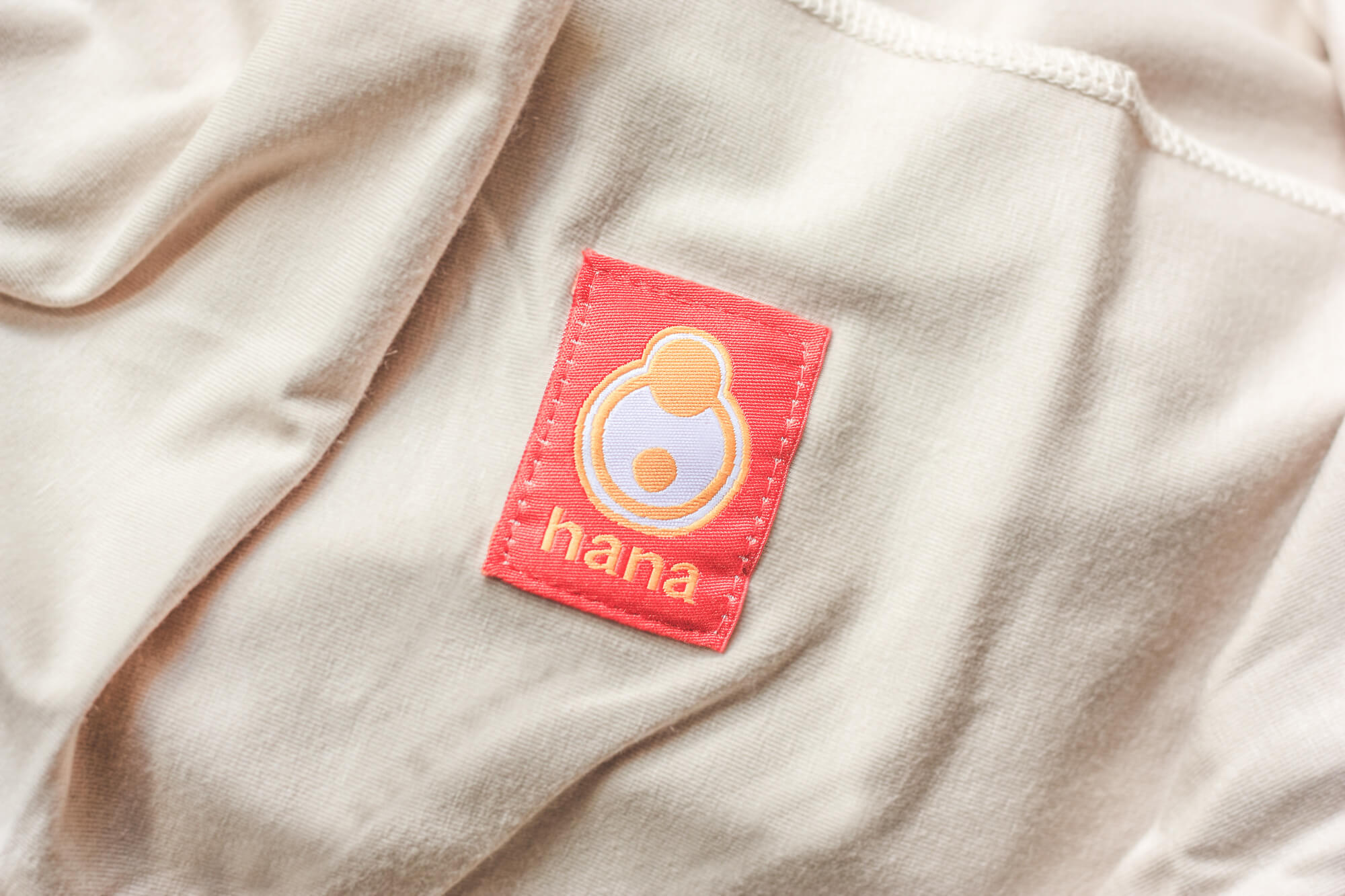 The image shows the Hana Baby Standard sling in the colour tan. Neatly folded flat